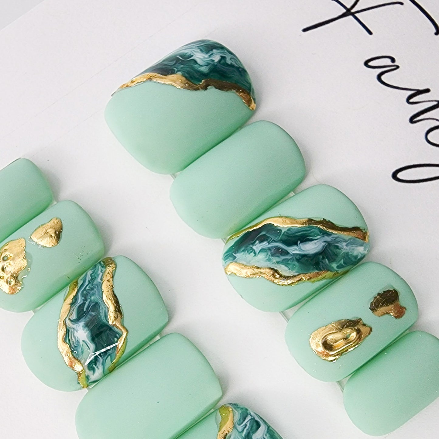 jasper and gold chrome press on nails with marble designs on a teal matte color, shown in short squoval.