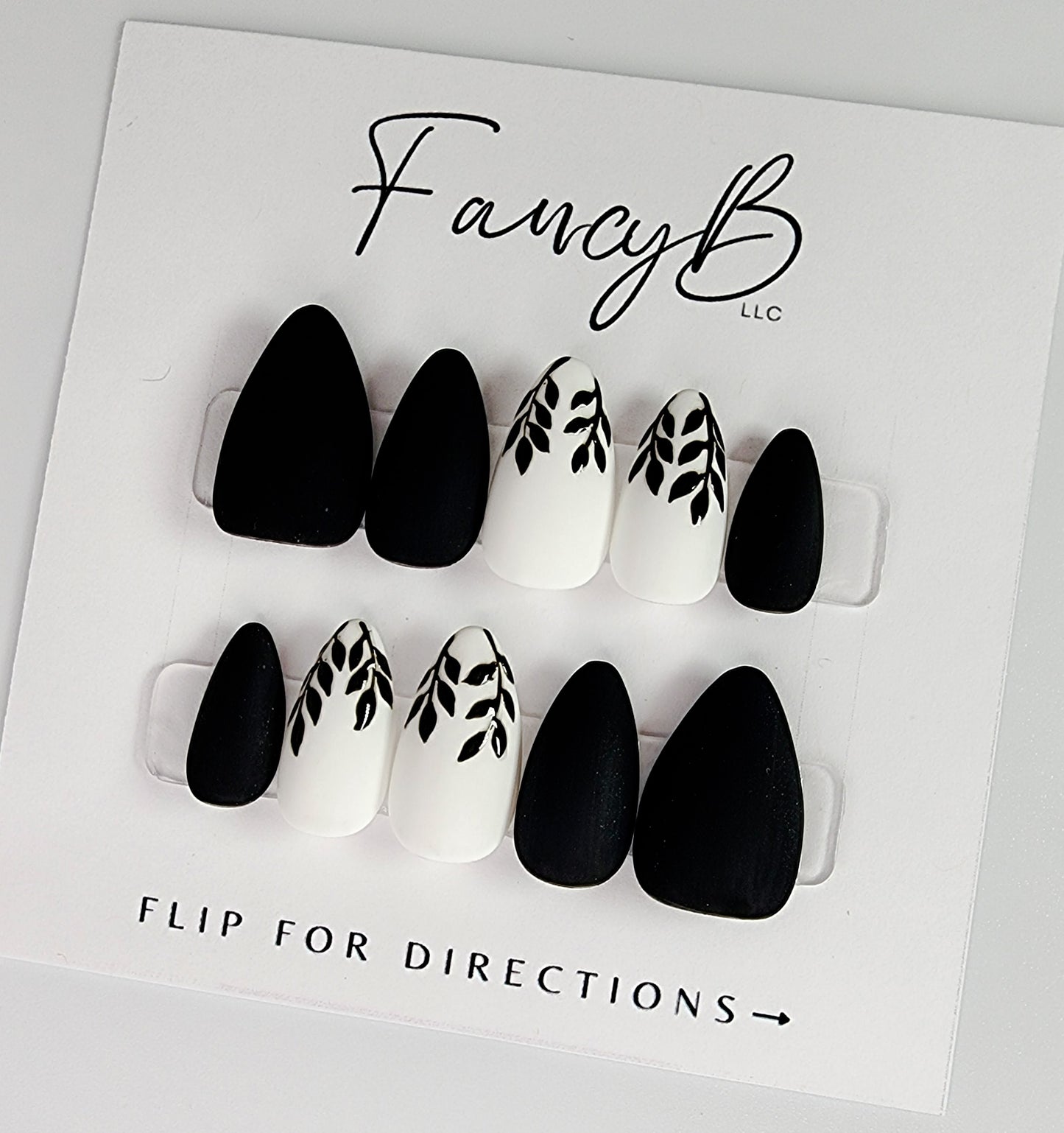 Custom press on nails, matte black and white with gloss black hand painted leaves in a short almond shape. FancyB Nails.