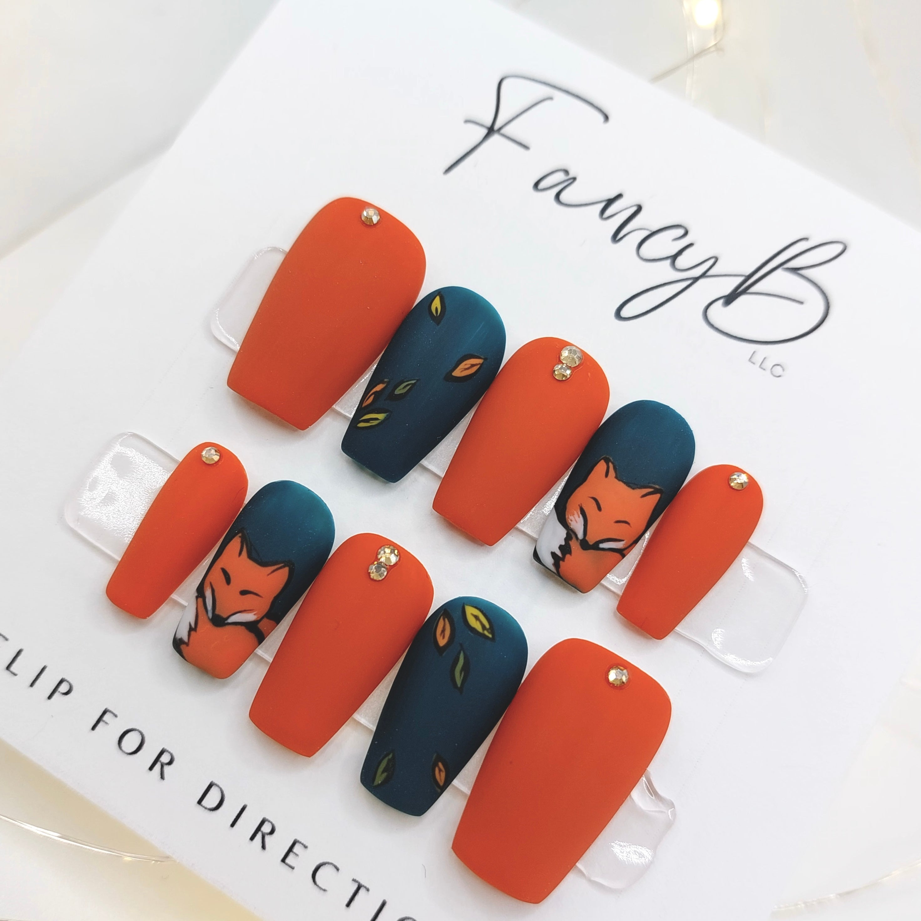 Custom press on nails, custom fox nails with hand painted foxes and leaves, gems, and orange and teal nail colors with matte finish on a short coffin shape. FancyB Nails.