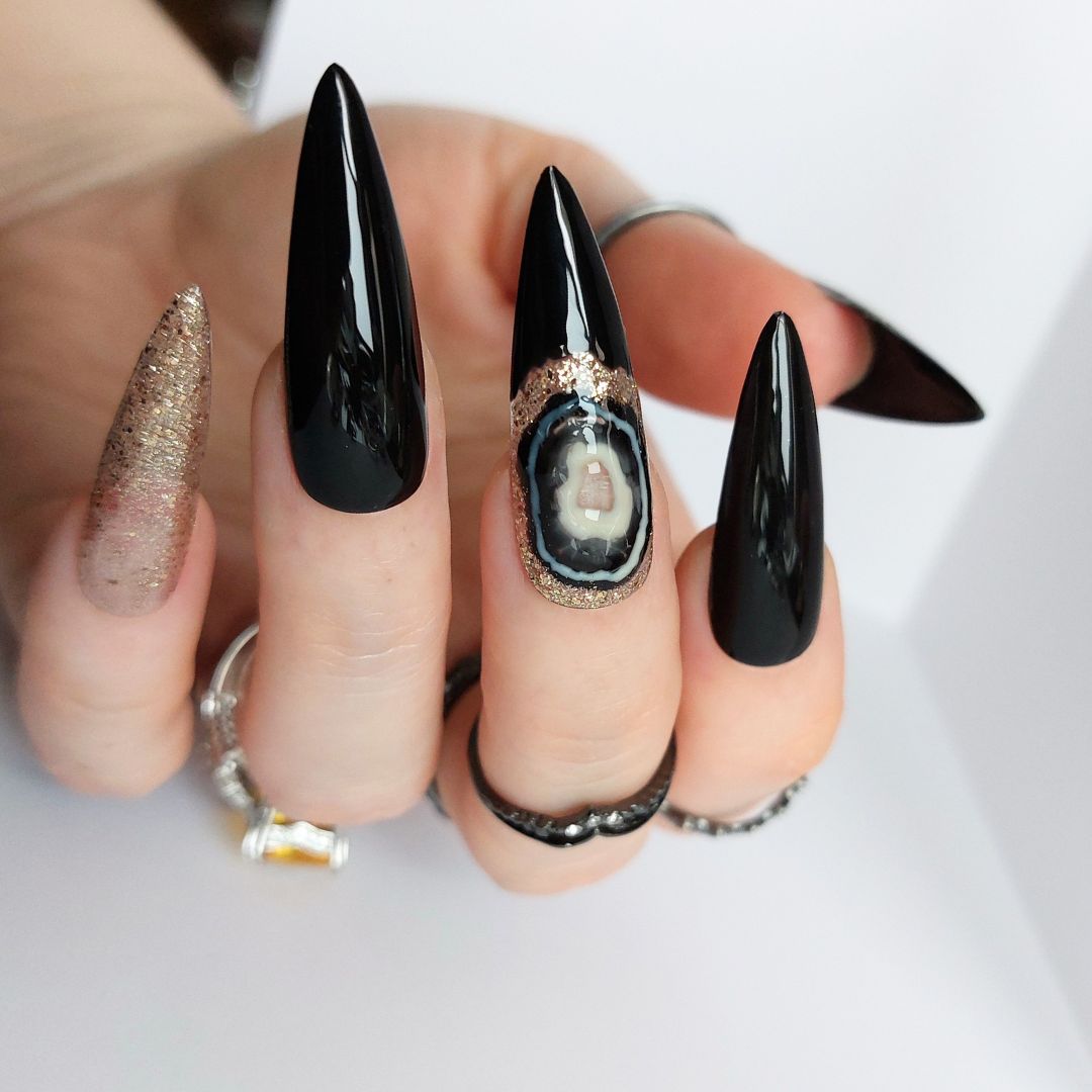 black agate nails with gold glitter and black accents, shown in sharpened long stiletto nails, handmade press on nails from fancyb nails. Gothic nail design ideas.