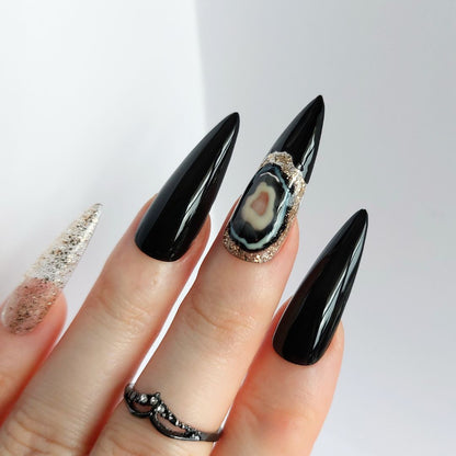 black agate nails with gold glitter and black accents, shown in sharpened long stiletto nails, handmade press on nails from fancyb nails. Gothic nail design ideas.