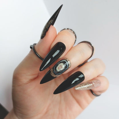 black agate nails with gold glitter and black accents, shown in sharpened long stiletto nails, handmade press on nails from fancyb nails. Gothic nail design ideas.