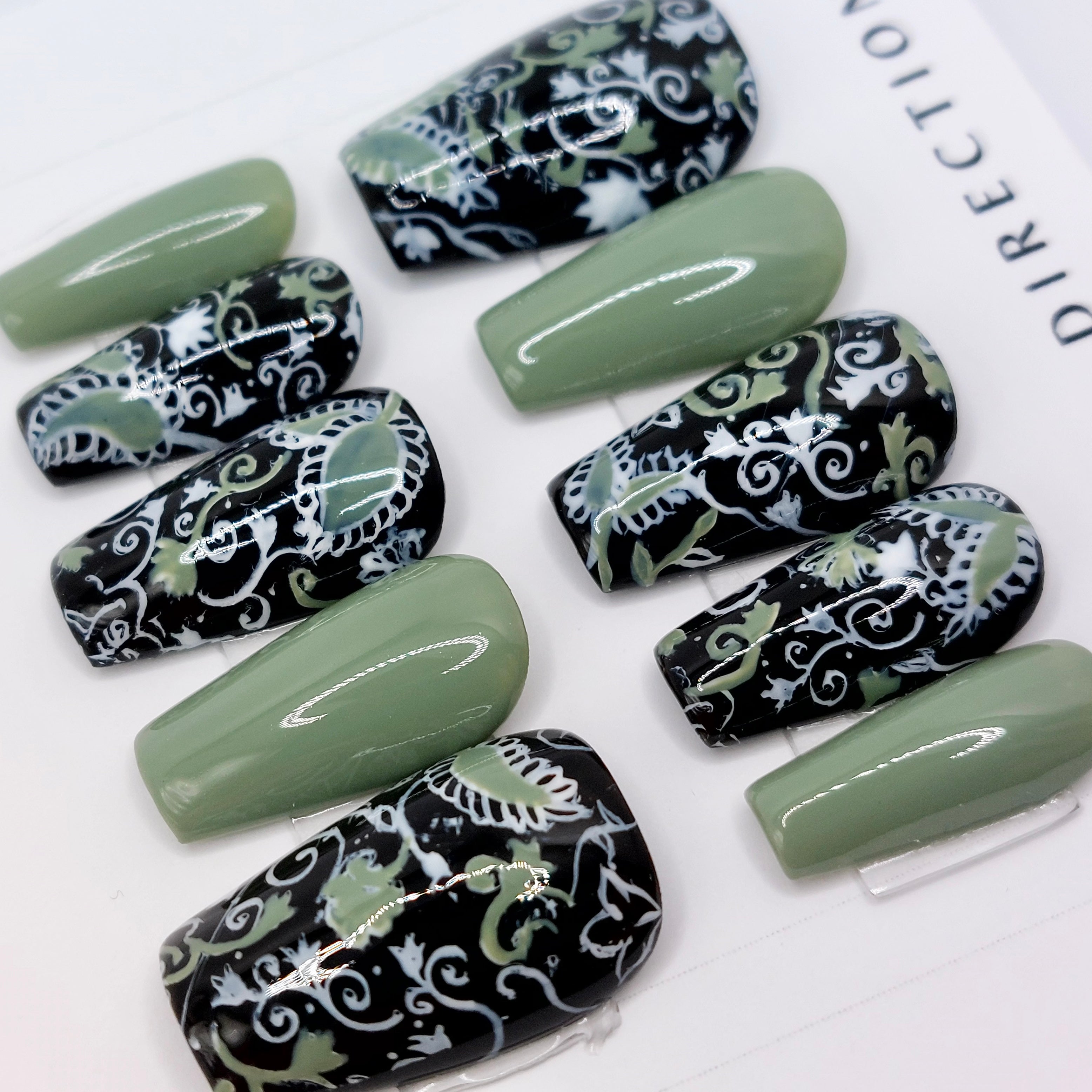 Custom press on nails, fancyb nails with white and sage floral designs on black background on short coffin press on nails.