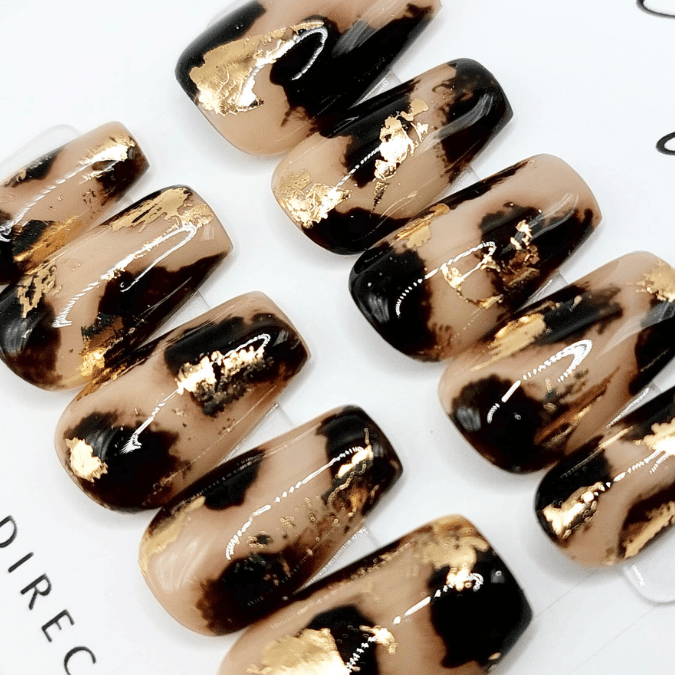 Custom tortoiseshell press on nails with layers of gel, light beige and black colors with gold flake accents in a short coffin shape. FancyB hand painted nails.