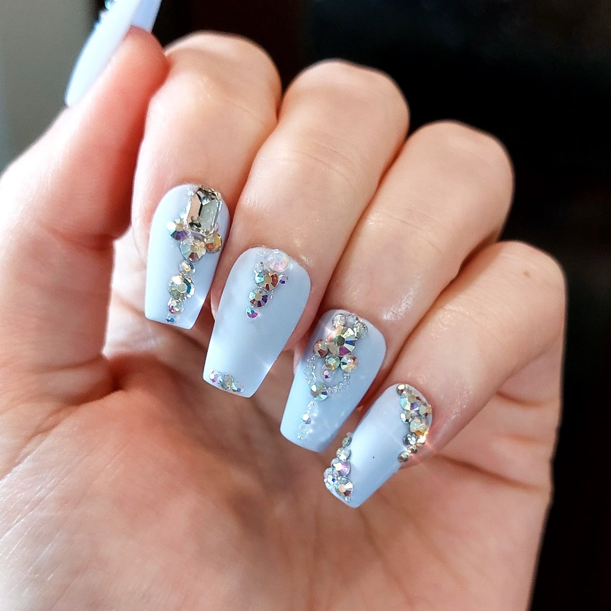 Periwinkle press on nails with a variety of crystals on a short coffin nail shape.