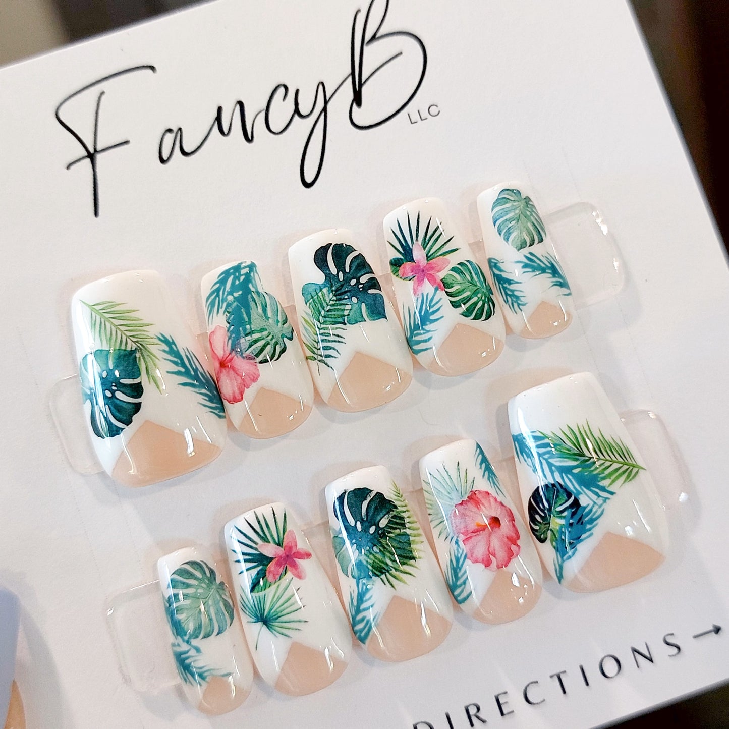Tropical press on nails with monstera leaves and palm leaves in fuscia and teal colors, a low french v-cut and short coffin nail shape.