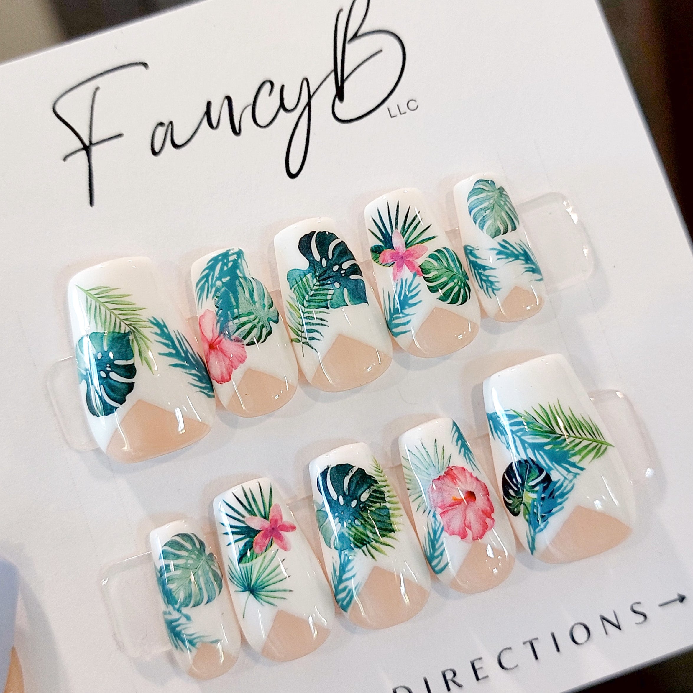 Custom press on nails. Tropical press on nails with monstera leaves and palm leaves in fuscia and teal colors, a low french v-cut and short coffin nail shape.
