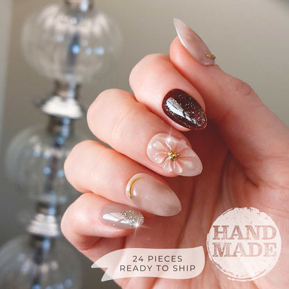 Spring floral press on nails with light pink 3d flowers, jelly gel, brown glitter accents, gold chrome details and silver glitter. Handmade press on nails from FancyB Nails show in short almond.