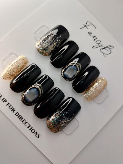 black agate press on nails with black nails and gold glitter, shown on medium square nails.