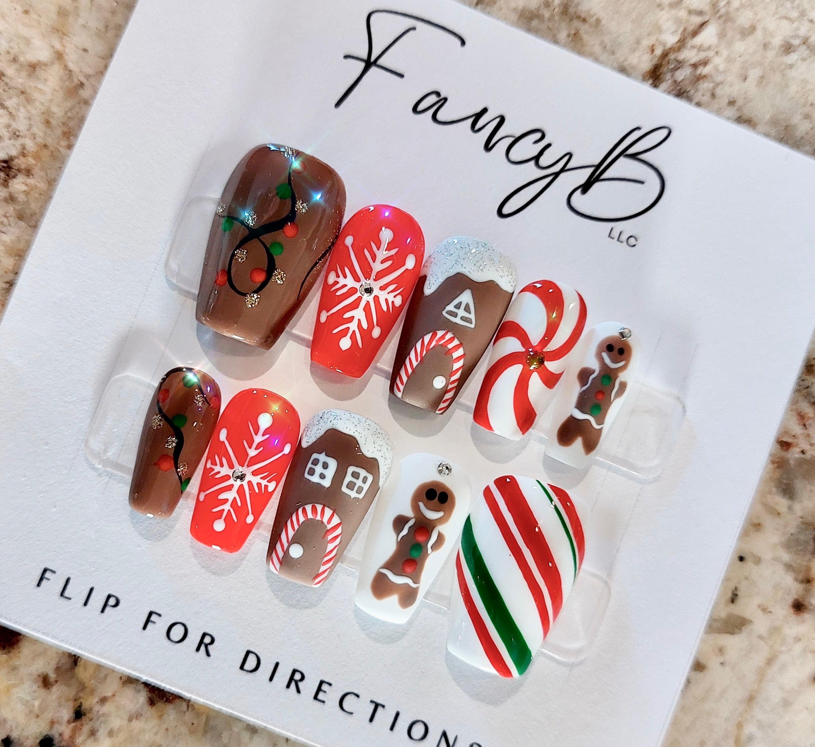 Custom Christmas Press on nails with gingerbread men, candycanes, gingerbread houses, snowflakes, and christmas lights on a short coffin shape. FancyB Nails.