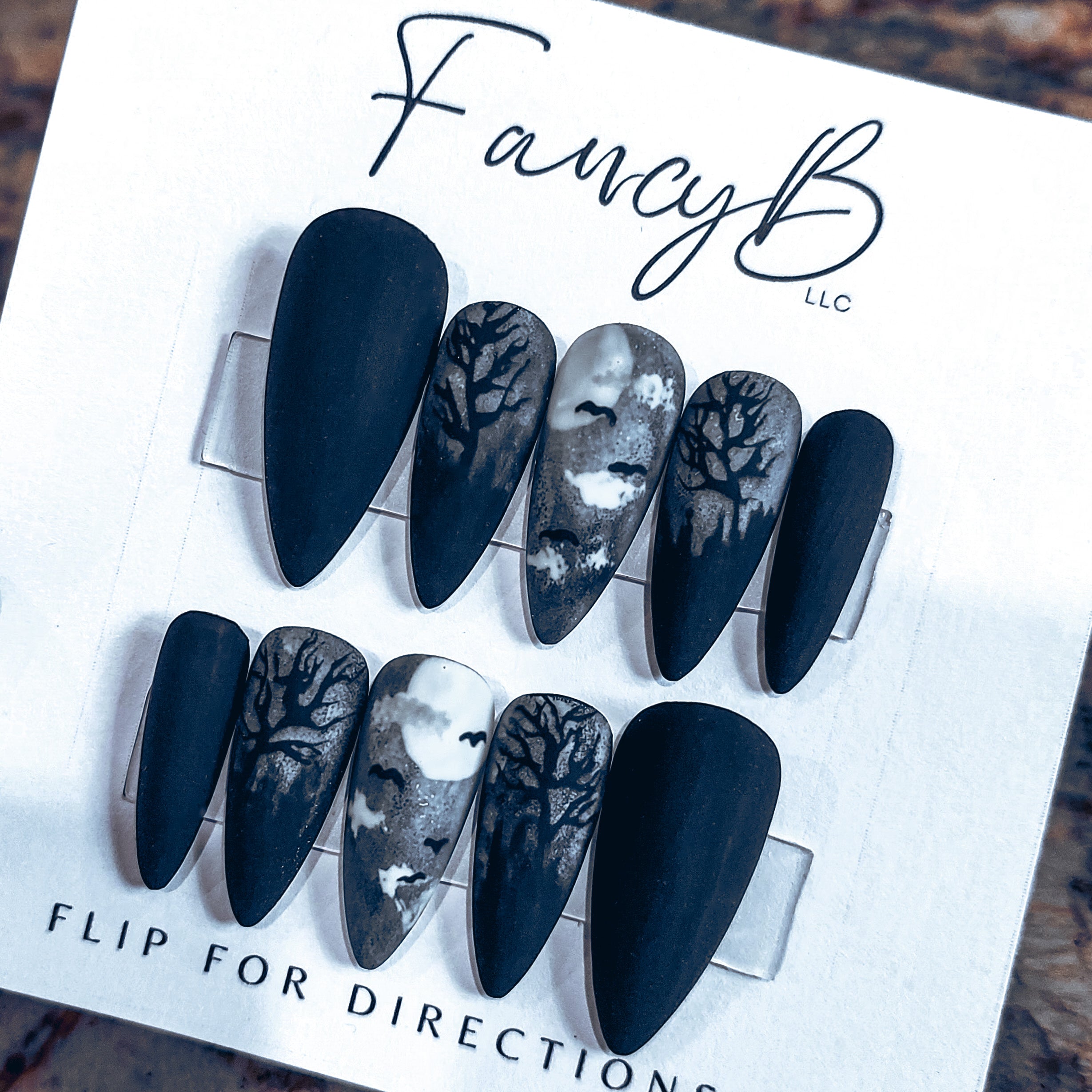 Custom Halloween press on nails with cemetery moonlight theme with bats and creepy tree outlines and matte finish all on a sharp stiletto nail shape. FancyB Nails.