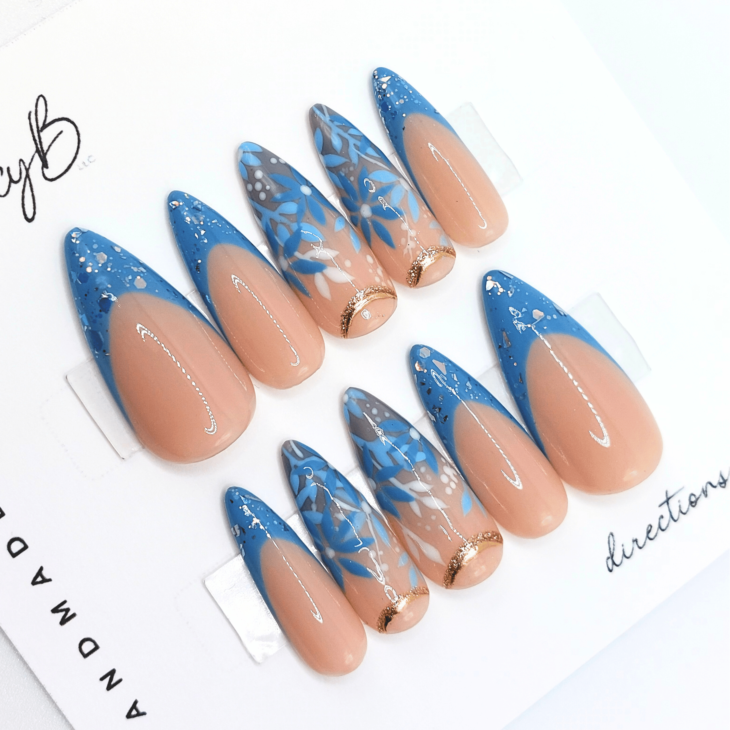 custom flower press on nails, hand painted floral designs in different shades of blue, in medium stiletto shape with nude base color.