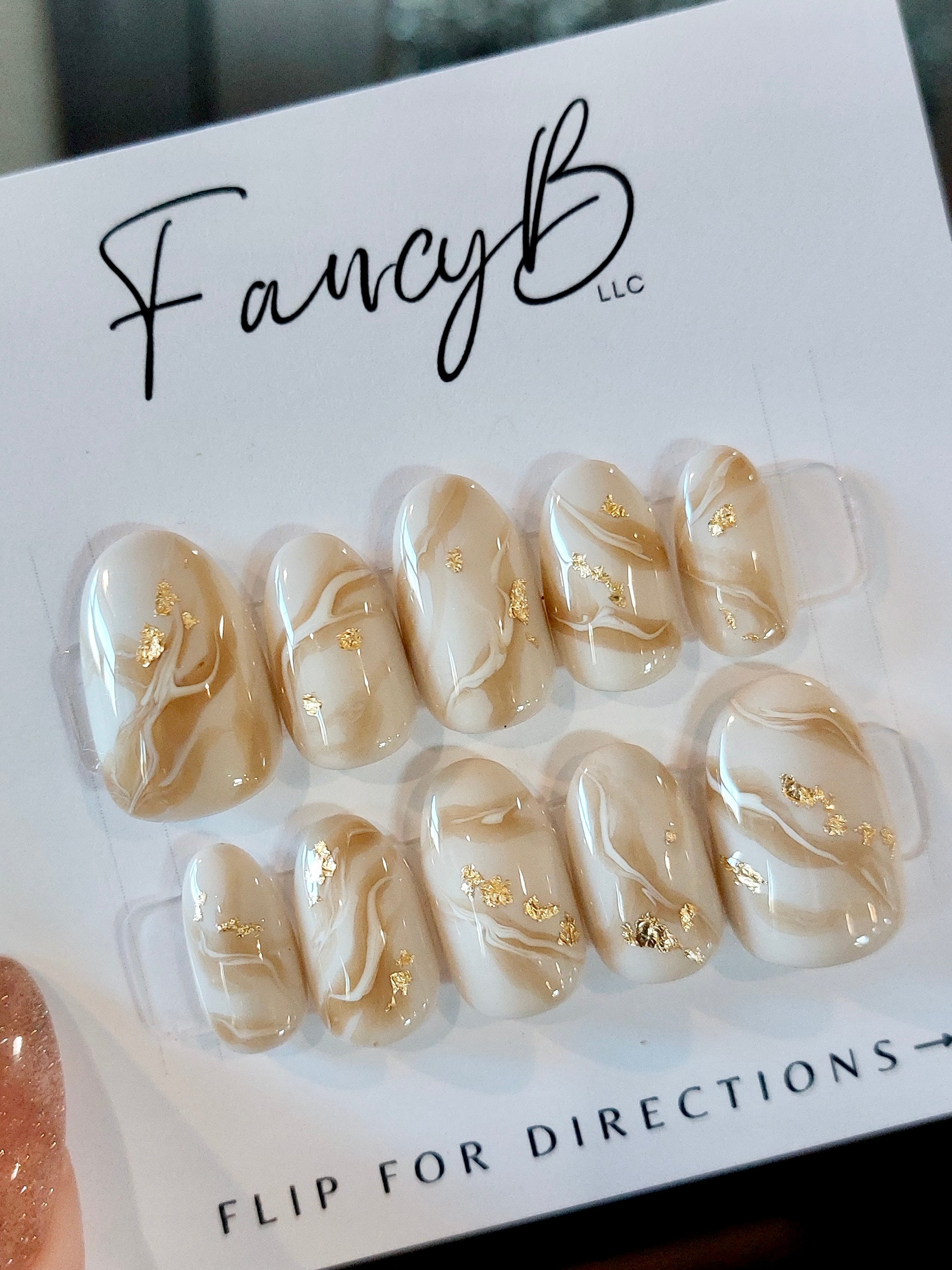 Custom press on nails fall caramel apple design with off white color and caramel swirls with gold flakes on a short oval nail shape. Fancyb Nails.
