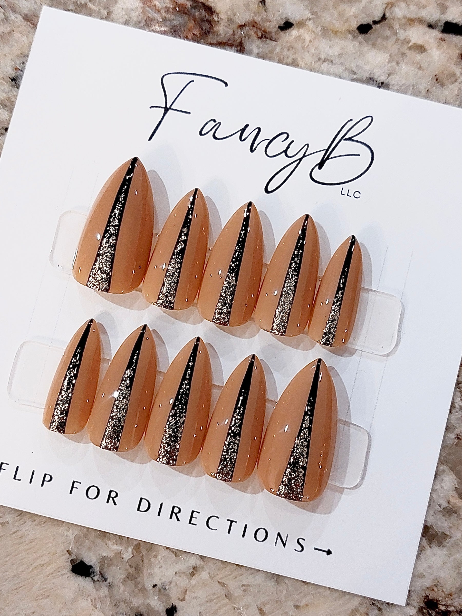 Custom press on nails with nude color and thin black lines down the middle with silver glitter and sharp short stiletto shape. FancyB Nails.