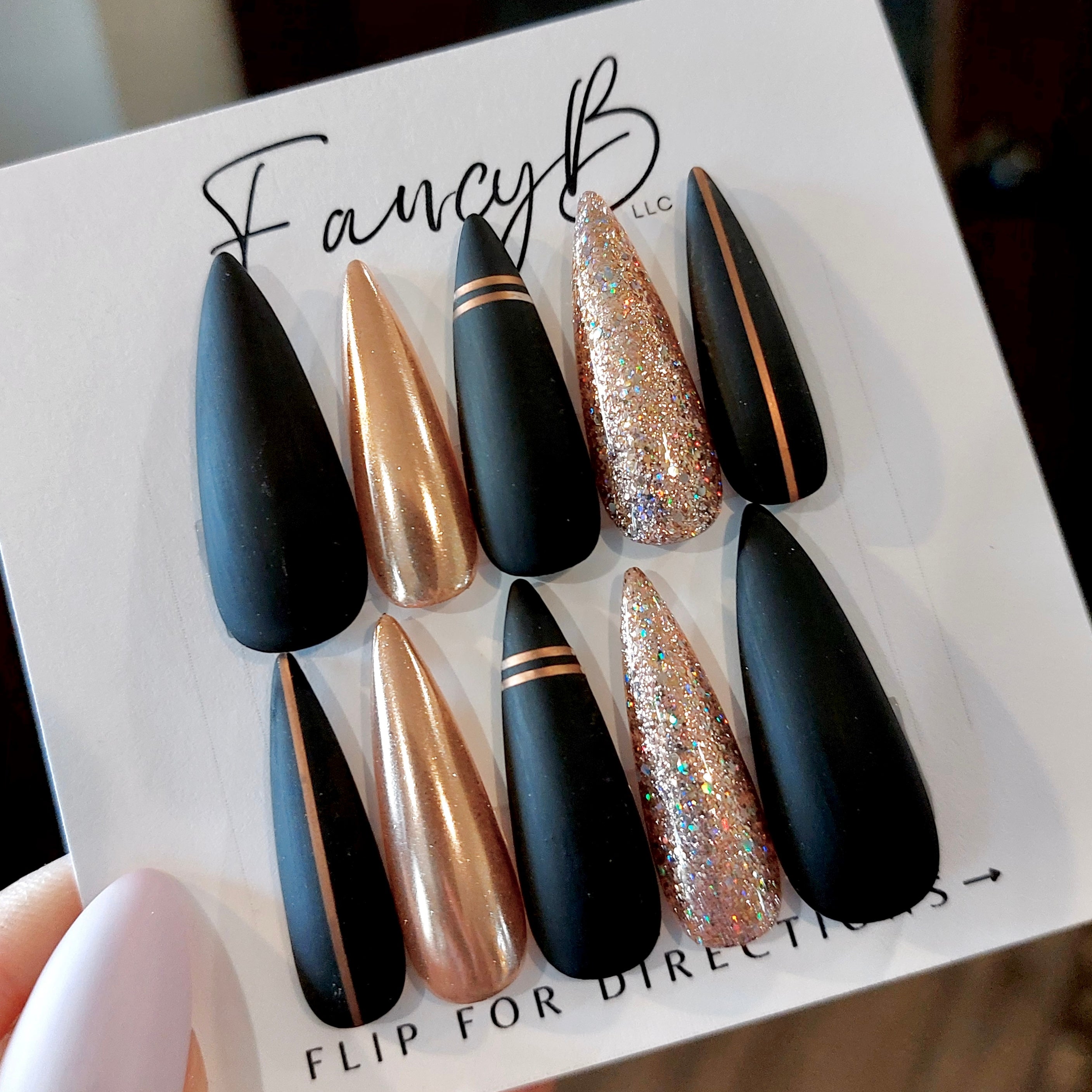 Custom press on nails matte black with rose gold chrome accents and rose gold glitter in a long stiletto shape. FancyB Nails.