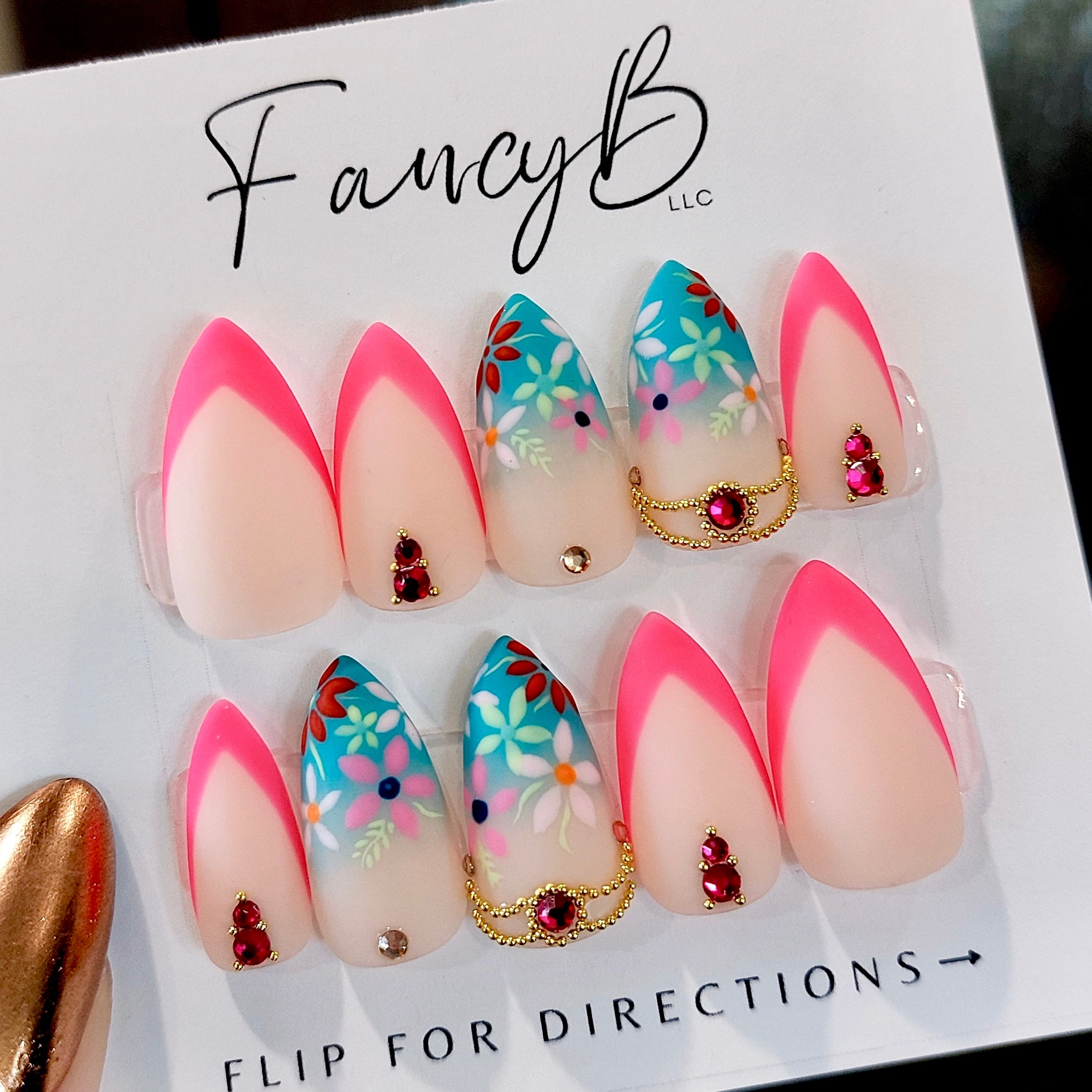 Custom press on nails with hand painted floral designs, hot pink french tips and blue teal ombre accents, ruby and pink gems and gold decorative pieces. Sharp short stiletto nail shape. FancyB Nails.