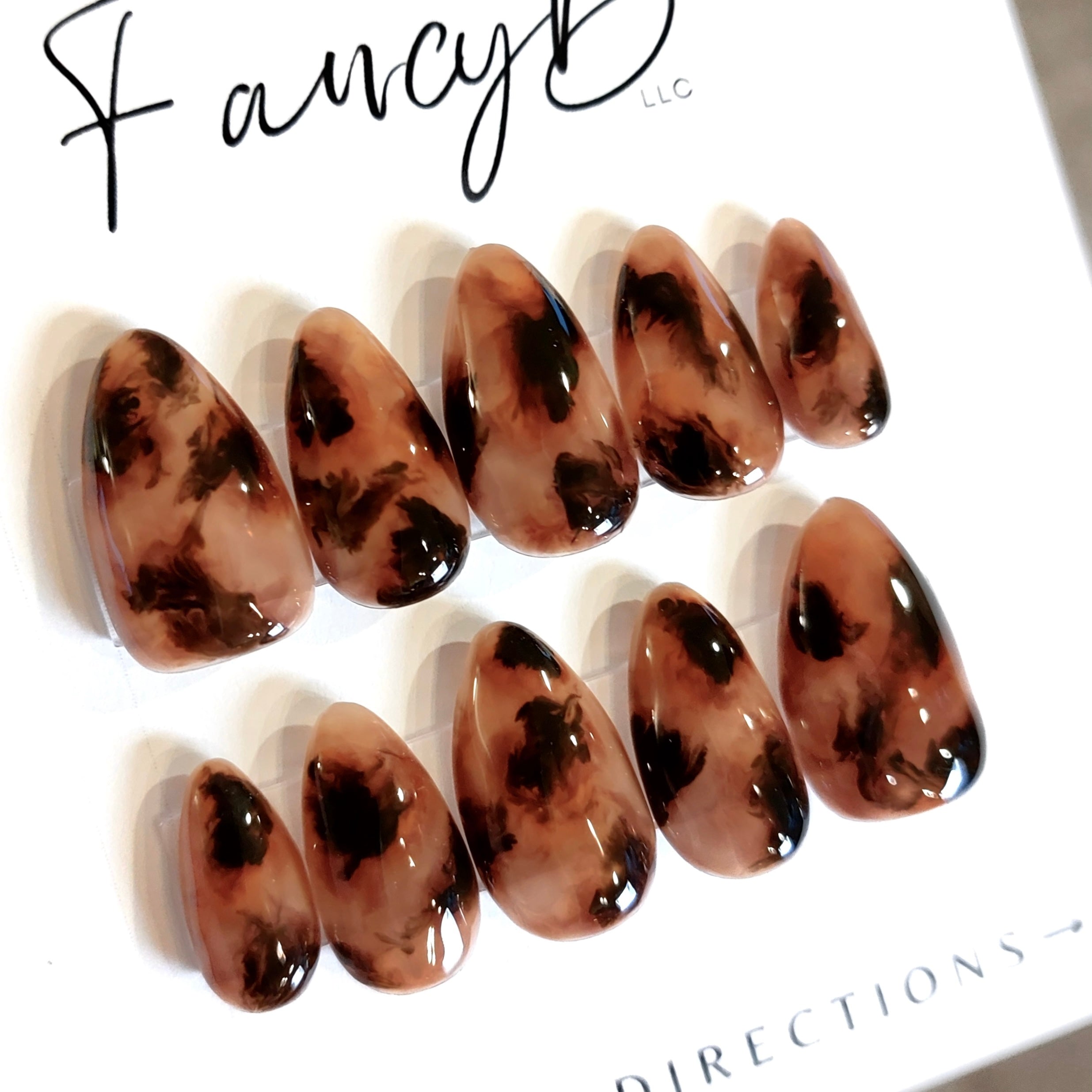 Custom press on nails in tortoiseshell design, medium brown color with deep brown and black spots in gloss finish with a short almond nail shape. FancyB Nails.