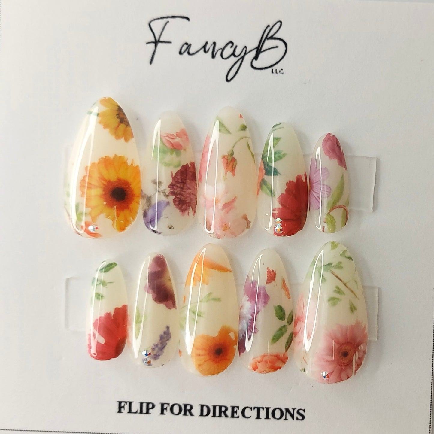 Milky Floral Press on Nail design adorned by some truly realistic flower designs in a long almond shape. Sunflowers, roses, carnations, peony, lilac nails.