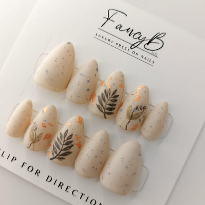 short almond press on nails with almond color and specks, hand painted leaves and rose gold flakes.