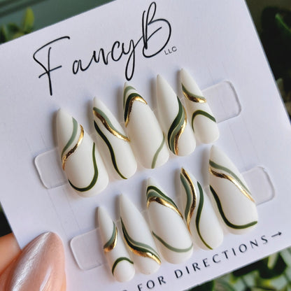 sage and olive green swirls, with gold chrome on a matte white finish. Sharp stiletto press on nail shape.