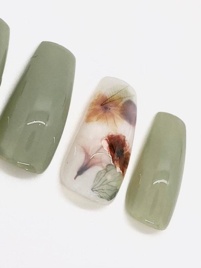 Sage milk bath press on nails with a milky white accent nail with leaves and flowers. Shown in a long coffin/ballerina shape.