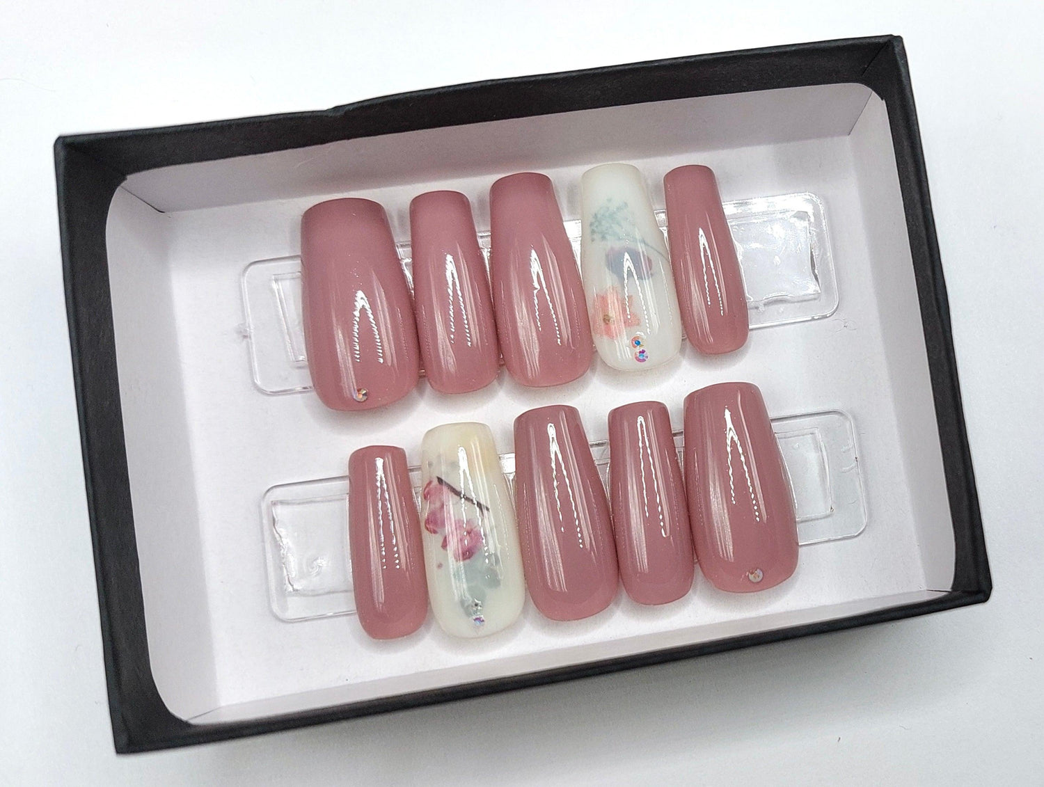 Dusty Rose milk bath press on nails with a milky white accent nail with leaves and flowers. Shown in a long coffin/ballerina shape.