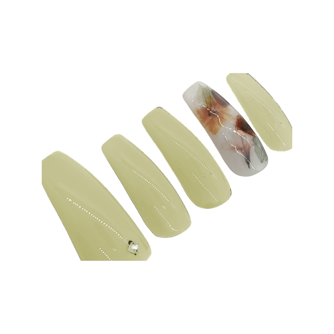 Soft yellow milk bath press on nails with a milky white accent nail with leaves and flowers. Shown in a long coffin/ballerina shape.