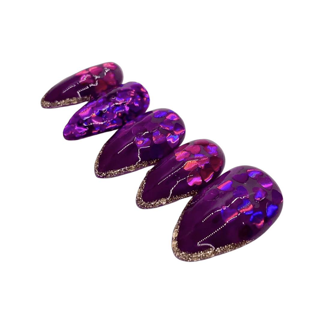 Gorgeous Valentine's Day press on nails that fade from a solid purple to a purple jelly tip, bordered with gold glitter. Each nail has purple heart glitter and a purple glitter accent nail. Shown in a short stiletto shape.