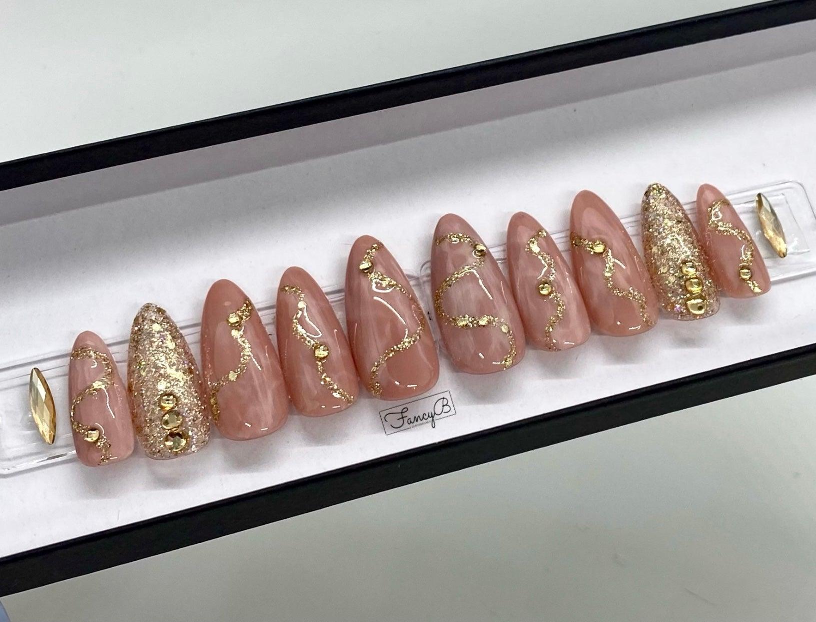 Custom nail design in a beautiful rose quartz design with gold glitter accents and gold gems all in a long almond shape.
