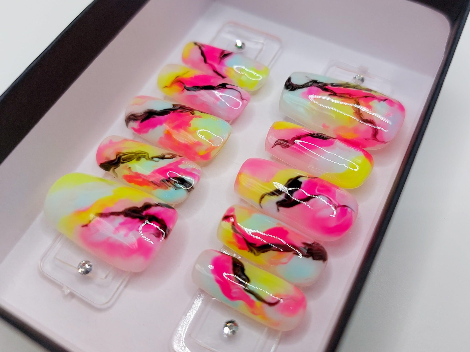 Vibrant colorful nails in neon pink, yellow, and blue with black lines. Tie dye marble designs.